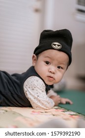 Asian Baby Boy Wearing Black Knitted Beanie Lying On Play Mat During Tummy Time At Home. Child Is 6 Months Old.