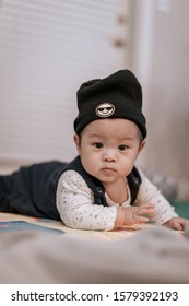 Asian Baby Boy Wearing Black Knitted Beanie Lying On Play Mat During Tummy Time At Home. Child Is 6 Months Old.