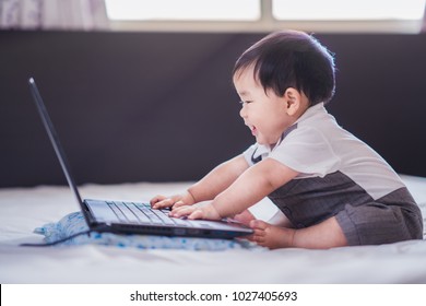 Asian baby in business suite sit and play computer notebook on the bed, this immage canuse for education, business, child, boy, internet, index, trchnology, easy, job and dream concept