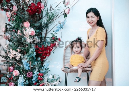 Asian baby daughter with mother wearing yellow dress in the park. Happy loving family. mother playing with her baby. Kid and mom are playing on the nature outdoors. Walk in the park.