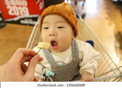 Asian Baby Eating Banana For Tasting On The Shopping Cart