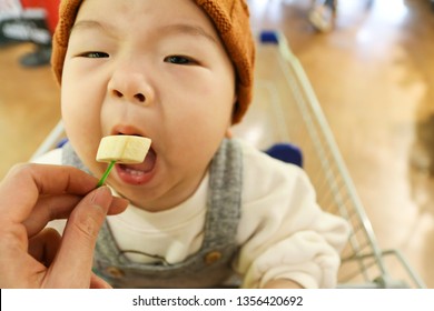 Asian Baby Eating Banana For Tasting On The Shopping Cart