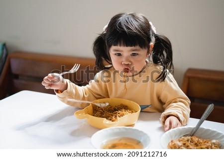 Asian baby eating delicious noodle in kitchen on dining table. Happy asian baby girl practice eating by her self on dining table. Baby lifestyle concept