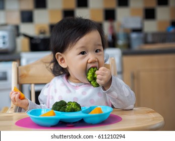 Asian Baby Girl Eating Vegetable At Home Kitchen