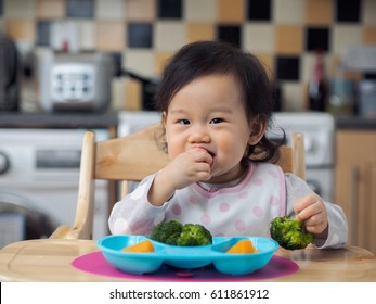 Asian Baby Girl Eating  Vegetable At Home Kitchen