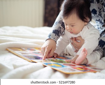 Asian Baby Girl Reading Book With Mom
