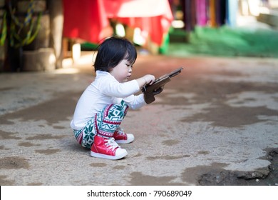 Asian baby girl sitting and playing wood gun.She ware white long shirt tile long leg and red shoes.