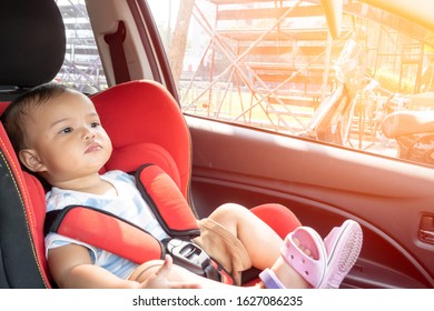 Asian baby girl sitting properly on a red car safety seat with sunlight from side window
