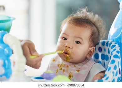 Asian Baby Girl Wearing Apron Eating Food And Mess Up On Her Face.