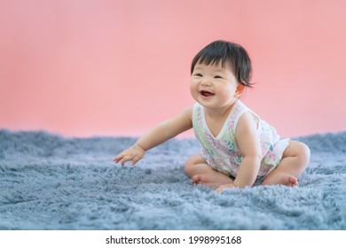 Asian Baby Smiling And Sitting On Carpet With Pink Color Background. Cute 6 Months Baby Sitting With Copy Space Use As Concept Of Valentine, Love, Learn, Education, Baby Or Kid Department In Hospital.