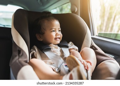 Asian Baby Toddler Girl Sitting In Car Seat And Looking Through Window. Infant Baby With Safety Belt In Vehicle. Safety Car. Family Travel Concept