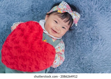 Asian Baby Valentine With Red Heart Smiling And Laying On Carpet. Cute 6 Months Baby Smling, Laughing And Laying Use As Concept Of Valentine, Love, Baby Or Kid Department In Hospital.