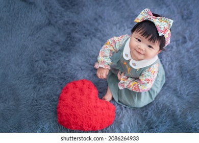 Asian Baby Valentine With Red Heart Smiling And Sitting On Carpet. Cute 6 Months Baby Smling, Laughing And Sitting Use As Concept Of Valentine, Love, Baby Or Kid Department In Hospital.