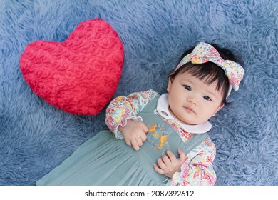 Asian Baby Valentine With Red Heart Smiling And Laying On Carpet. Cute 6 Months Baby Smling, Laughing And Laying Use As Concept Of Valentine, Love, Baby Or Kid Department In Hospital.