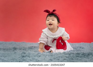 Asian Baby Valentine With Red Heart Smiling And Sitting On Red Background. Cute 6 Months Baby Sitting With Copy Space Use As Concept Of Valentine, Love, Baby Or Kid Department In Hospital.