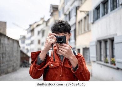 Asian backpacker use camera taking a picture of beautiful landscape. Young male tourist traveler travel alone on street in city, using cellphone record vlog on holiday vacation trip in Switzerland.
