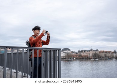 Asian backpacker use camera taking a picture of beautiful landscape. Young male tourist traveler travel alone on street in city, using cellphone record vlog on holiday vacation trip in Switzerland.