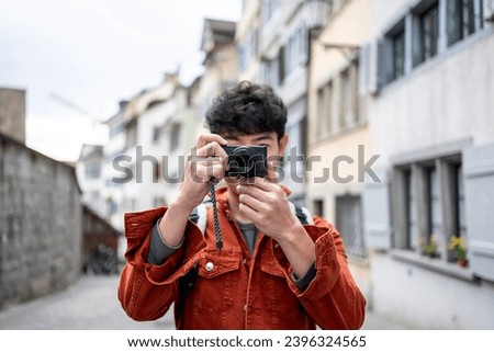 Asian backpacker use camera taking a picture of beautiful landscape. Young male tourist traveler travel alone on street in city, using cellphone record vlog on holiday vacation trip in Switzerland.
