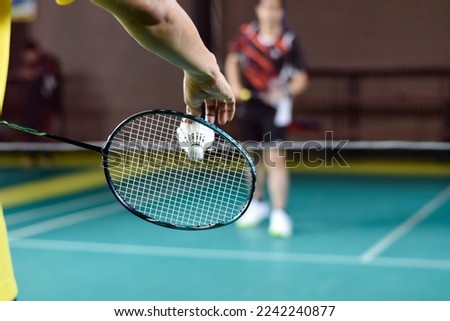 Asian badminton player holds racket and white cream shuttlecock in front of the net before serving it to another side of the court.