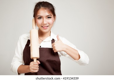 Asian Baker Woman  In Apron   Thumbs Up  With Wooden Rolling Pin On Gray Background