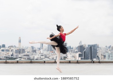 Asian ballerina ballet girl in red, black dress dancing on rooftop with cityscape view background. Young ballerina ballet girl dancing by stretching arms and leg on rooftop - Powered by Shutterstock