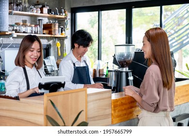 Asian Barista Or Coffee Maker Receive The Order From Customer Woman While Her Co-worker Prepare Coffee By Machine. Concept Of Good Teamwork Support Small Business System.