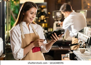 Asian Barista Make Payment With Customer Credit Card Using  EMV Chip Technology For Coffee Purchase At A Cafe Bar.