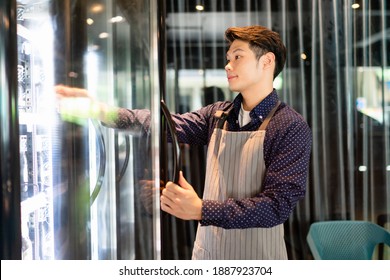 Asiatischer Barista Mann, der die Tür im Café reinigt, um den Ausbruch von Covid-19 zu verhindern.