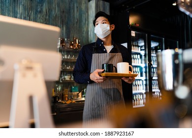 Asian Barista Man Wearing Mask Serving Coffee In Cafe. Reopen Business After Covid-19 Outbreak Concept.