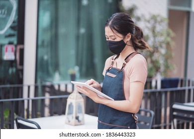 Asian Barista Woman Worker New Normal Wearing Facemask Protection COVID-19 Coronavirus Pandemic Using Smart Tablet Device Customer Service Serving Food At Café Restaurant Store Small Business Owner