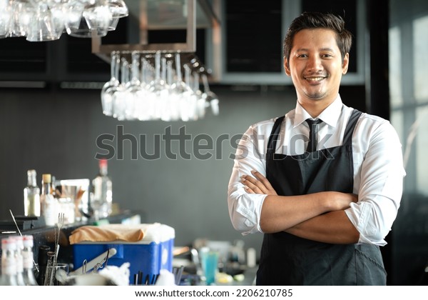 Asian bartender man standing at bar counter\
prepare to service cocktail alcohol at restaurant, portrait.\
Handsome young barman in uniform working at bar - drink\
establishment. Nightlife\
lifestyle.