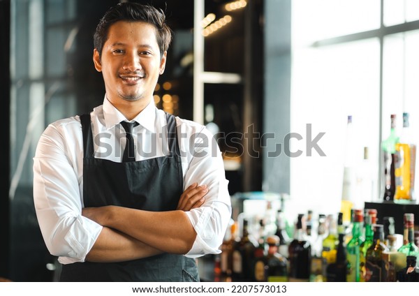 Asian bartender man standing at bar counter\
prepare to service cocktail alcohol at restaurant, portrait.\
Handsome young barman in uniform working at bar - drink\
establishment. Nightlife\
lifestyle.