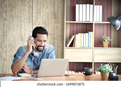 Asian Bearded Business Owner Holding Earphones At The Ear While Looking At The Laptop Being Video Conference Happily. Warm Father Having A Video Call With Daughter In A Foreign Country.