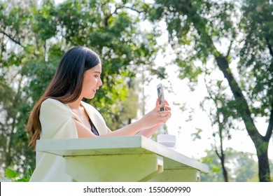 Asian Beautiful Business Woman Use Mobile Phone To Selfie Or Facetime To Contact With Other People And Work In The Garden.