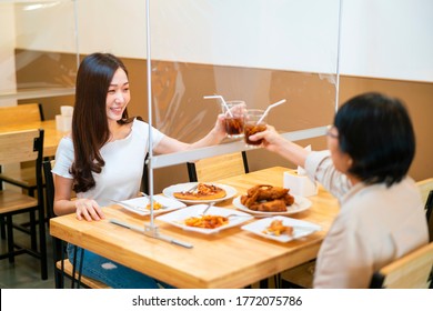 Asian beautiful female clinking a glass of water with her mother who siting separate and keep distance with table plastic shield partition in restaurant, new normal and social distancing concept - Shutterstock ID 1772075786
