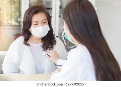 Asian Beautiful Female Doctor Uses Stethoscope To Check Health Of Lungs And Heart Or Diagnosis Symptom Of Woman Elderly Patient While Both Wear Face Mask In Hospital.