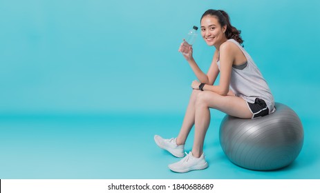 Asian beautiful happy woman holding water bottle and sitting on fit ball after exercise isolated on blue colour background.Concept of slim and healthy girl workout. - Powered by Shutterstock