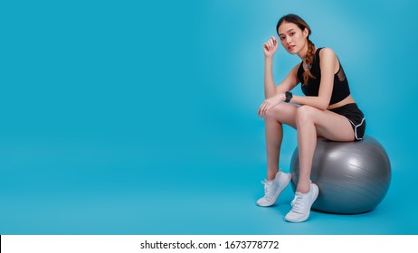 Asian Beautiful Happy Woman Wearing Smart Watch And Sitting On Fit Ball After Exercise Isolated On Blue Color Background.Concept Of Slim And Healthy Girl Workout.