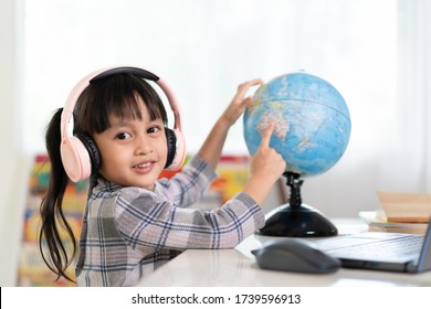 Asian Beautiful Little Student Girl Is Smiling And Pointing On Bilingual Globe Model For Her Online Lesson, Concept Of Learn From Home And Homeschooling For Child Education In The Outbreak Of Covid 19