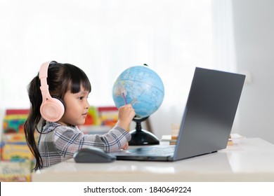 Asian Beautiful Little Student Girl Is Smiling And Pointing On Bilingual Globe Model For Her Online Lesson, Concept Of Learn From Home And Homeschooling For Child Education In The Outbreak Of Covid 19