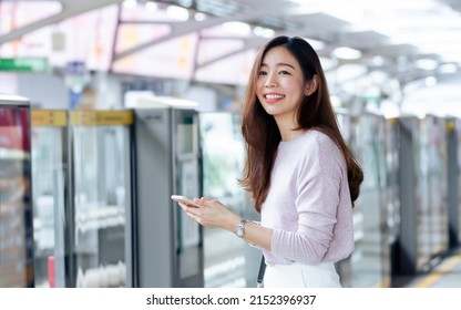 Asian beautiful long hair woman smiling with happiness and refresh, wearing casual business shirt, holding mobile phone, standing on platform, waiting for sky train transportation in morning day - Powered by Shutterstock