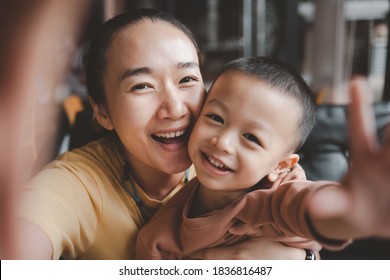 Asian Beautiful Mother And Child Happily Beautiful Young Mom And Cute Little Boy Are Sitting Together, Using A Smart Phone And Smiling And Take Selfie.