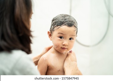 Asian Beautiful Mother Holding Little Cute Baby And Taking A Bath Her Child Sitting In Bathtub In The Room. Bubble Soap Shampoo On Kid Hair. Little Girl Looking At Camera. Clean And Healthy Concept.