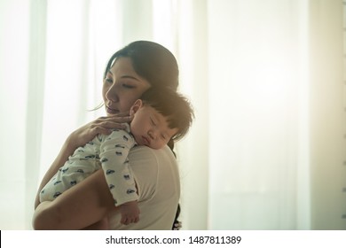 Asian Beautiful Mother Hugging Sleeping Baby In Her Arms And Kissing The Kid Gently. The Mom Closing Her Eyes While Holding Her Baby Head To Rest On Shoulder. Touch Of Love And Family Relationship.