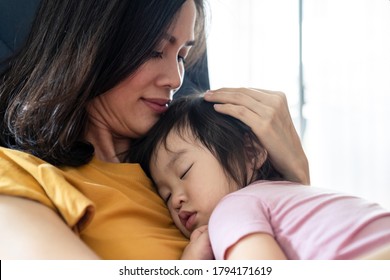 Asian Beautiful Mother Hugging Sleeping Baby In Her Arms And Kissing The Kid Gently. The Mom Closing Her Eyes While Holding Her Baby Head To Rest On Shoulder. Touch Of Love And Family Relationship.