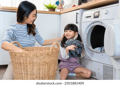 Asian beautiful mother teach young daughter wash dirty clothes at home. Adorable little cute girl child help and learn from parent mom to put laundry in washer appliance at home. Domestic-Housekeeping - Powered by Shutterstock