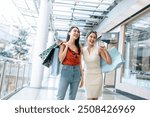 Asian beautiful two women shopping goods outdoor in department store. Attractive young female friend holding shopping bags, standing with happiness enjoy purchasing in shopping mall center together.