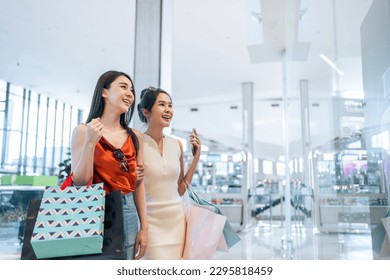 Asian beautiful two women shopping goods indoors in department store. Attractive young female friend holding shopping bags then walking with happiness enjoy purchasing in shopping mall center together