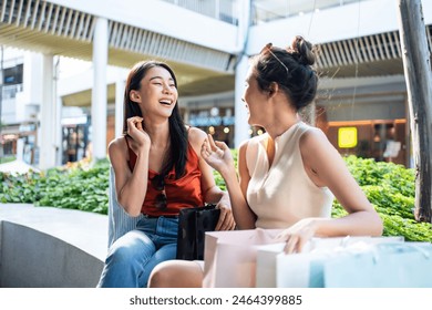 Asian beautiful two women shopping goods outdoor in department store. Attractive young female friend hold shopping bags sitting outside with happiness enjoy purchasing in shopping mall center together - Powered by Shutterstock