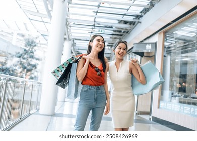 Asian beautiful two women shopping goods outdoor in department store. Attractive young female friend holding shopping bags, standing with happiness enjoy purchasing in shopping mall center together. - Powered by Shutterstock